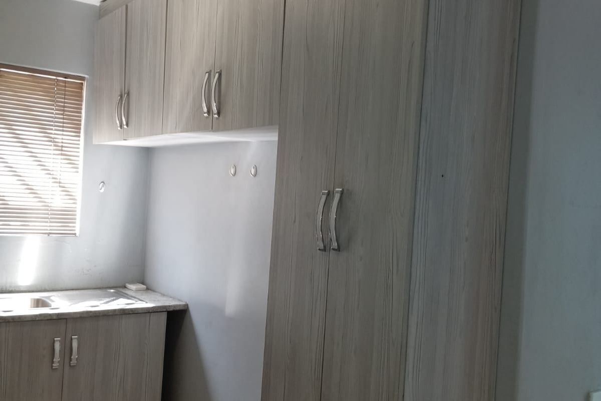 A functional kitchen area featuring light wood-grain built-in cabinetry, laminate countertops, a stainless steel sink, and tiled flooring.