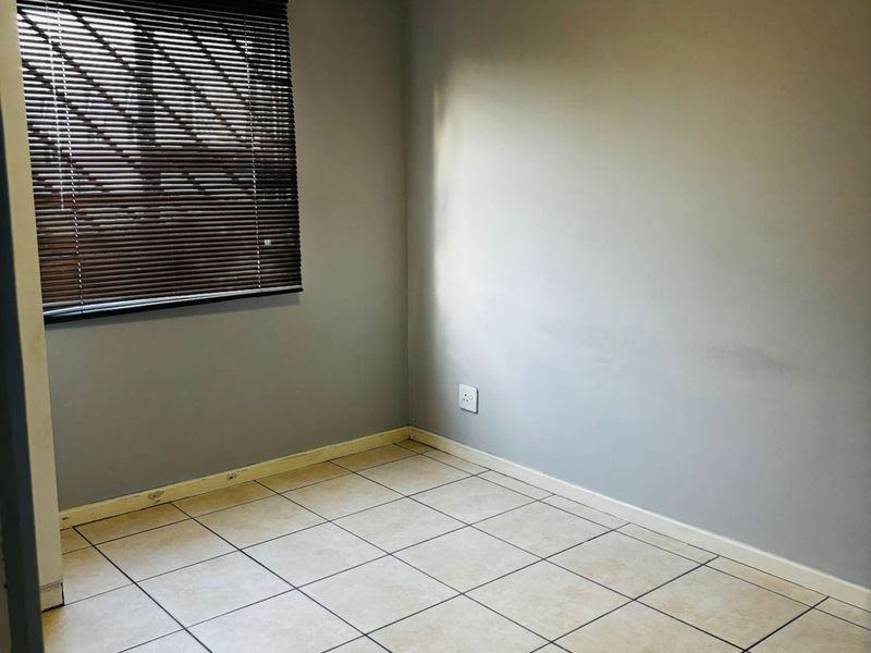 An empty bedroom featuring neutral tiled flooring, grey walls, and fitted venetian blinds, offering a blank canvas for personalization.