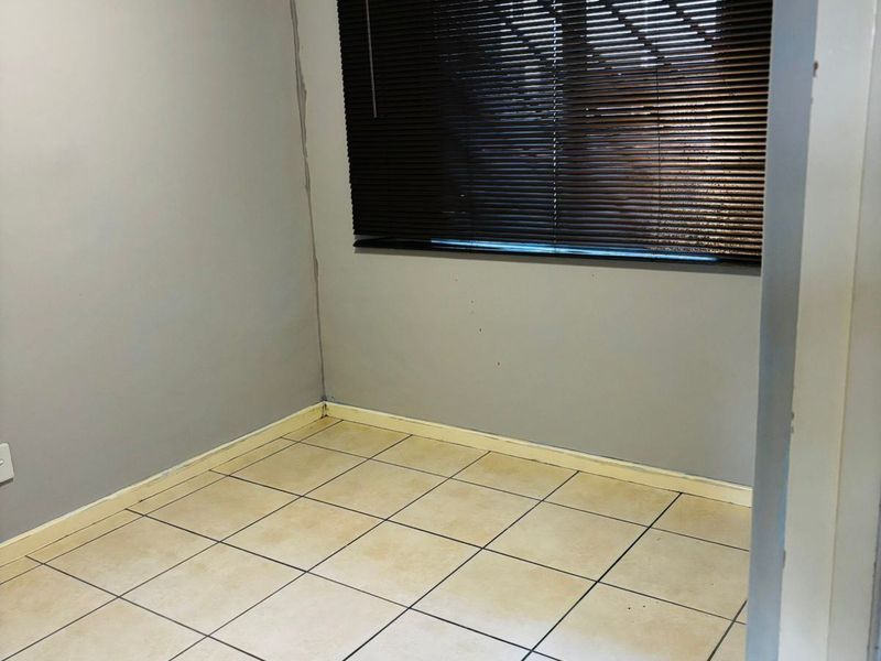 An empty bedroom featuring tiled flooring and dark venetian blinds, requiring minor cosmetic repairs and updates to the wall finishes and flooring.