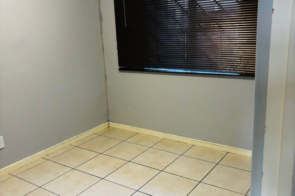 An empty bedroom featuring tiled flooring and dark venetian blinds, requiring minor cosmetic repairs and updates to the wall finishes and flooring.