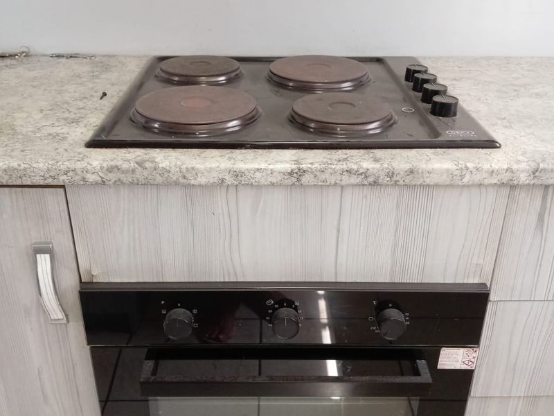 A clean kitchen section featuring a built-in Defy oven and electric hob set into a laminate countertop with modern wood-grain cabinetry.