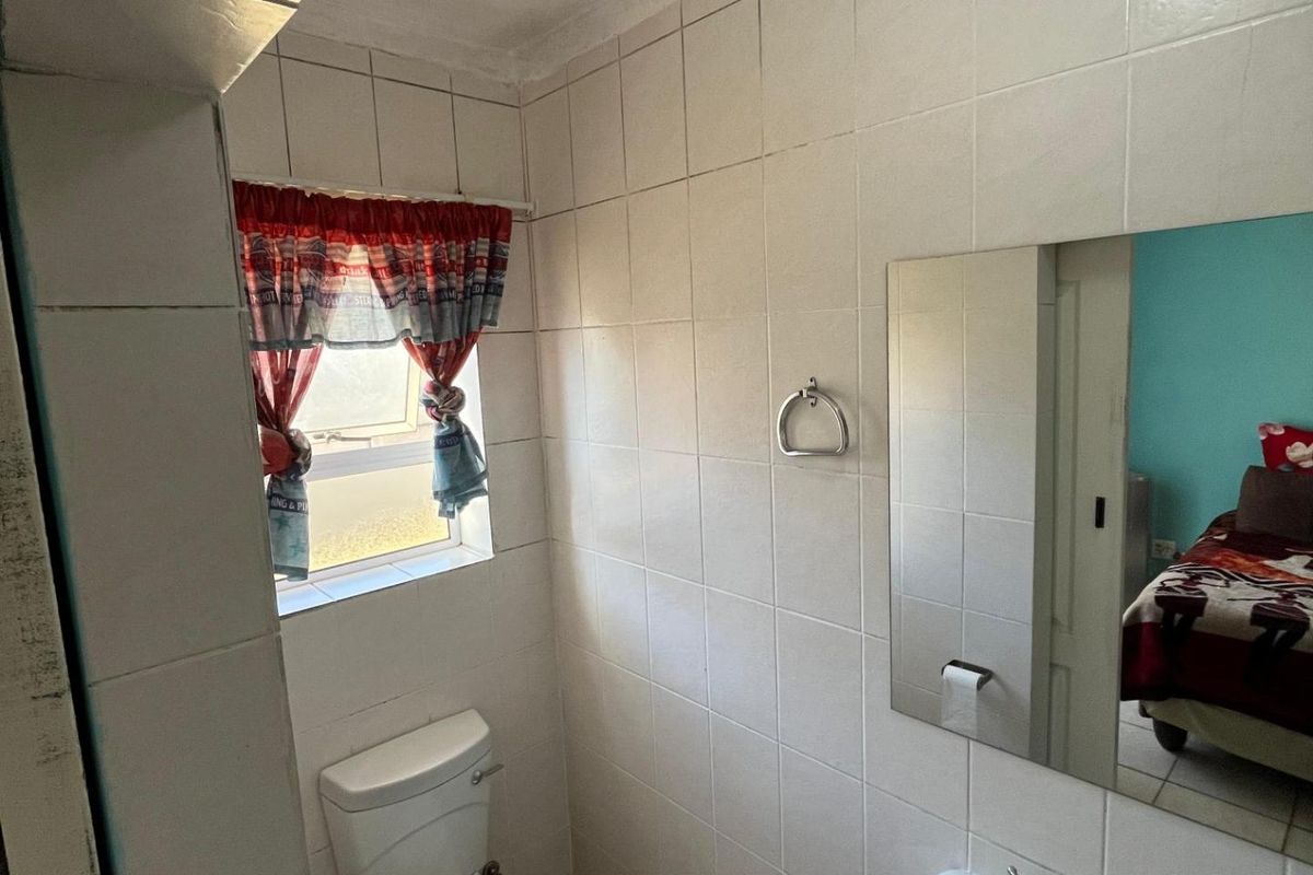 A compact bathroom featuring white wall tiles, a pedestal basin, a toilet, and a wall-mounted mirror.