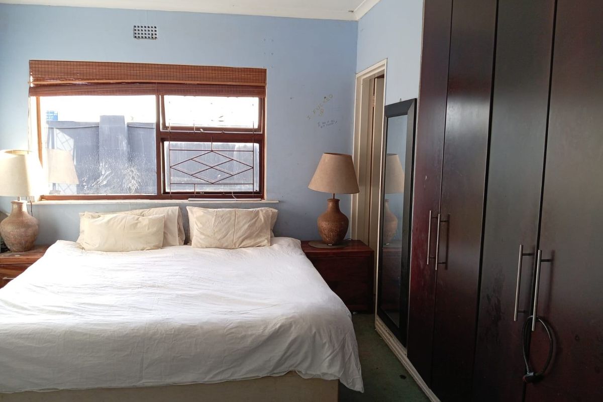 A bedroom featuring built-in dark wood wardrobes, a window with security bars, and a ventilation vent.