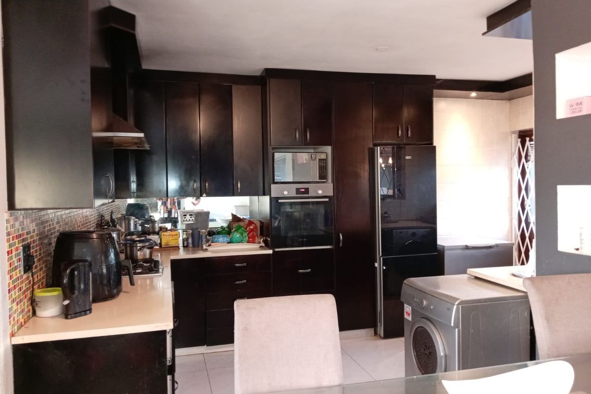 A functional kitchen featuring dark cabinetry, built-in oven, microwave, and integrated laundry space with tiled flooring.