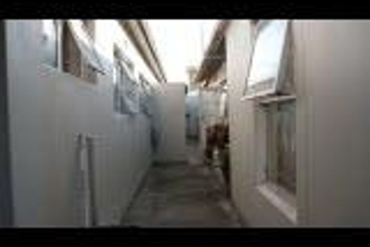A narrow side passage or exterior walkway between two sections of the property featuring concrete paving and multiple casement windows.