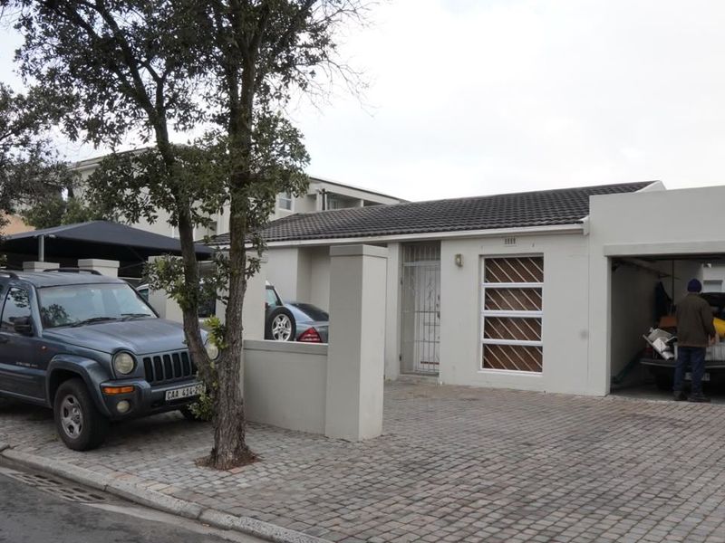 Front exterior view of a single-story house featuring a paved driveway, carport, and secure entrance with security gates and bars.