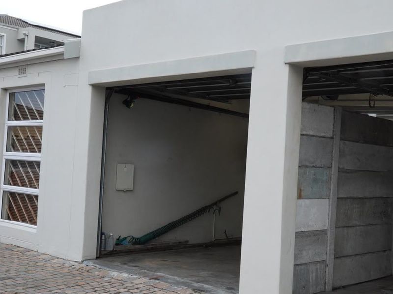A double garage with a paved driveway, featuring clean white exterior walls, aluminium window frames, and a secure entrance gate.