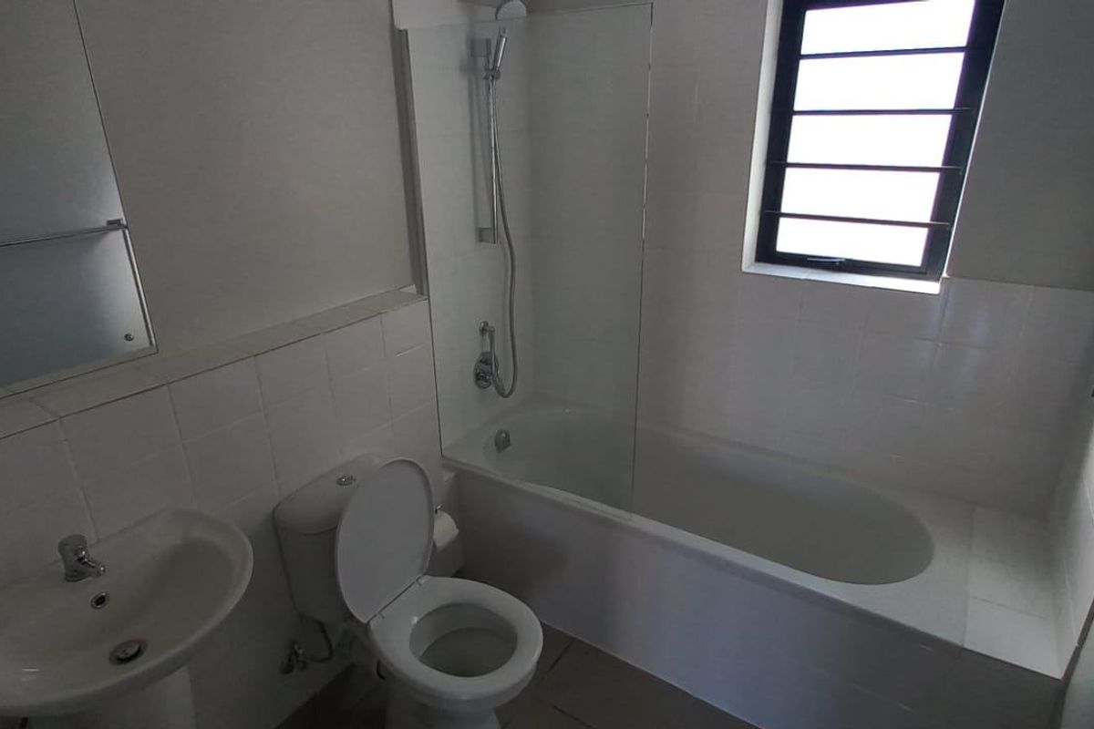 A functional bathroom featuring a pedestal basin, a toilet, and a bathtub with an integrated shower head and glass screen.