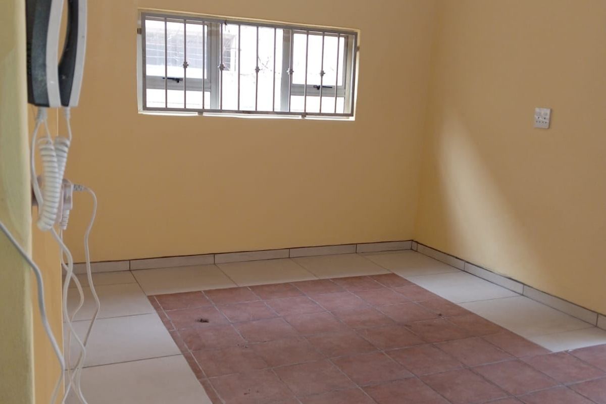 An empty living area featuring tiled flooring, security bars on the window, and a timber ceiling, providing a blank canvas for interior design.
