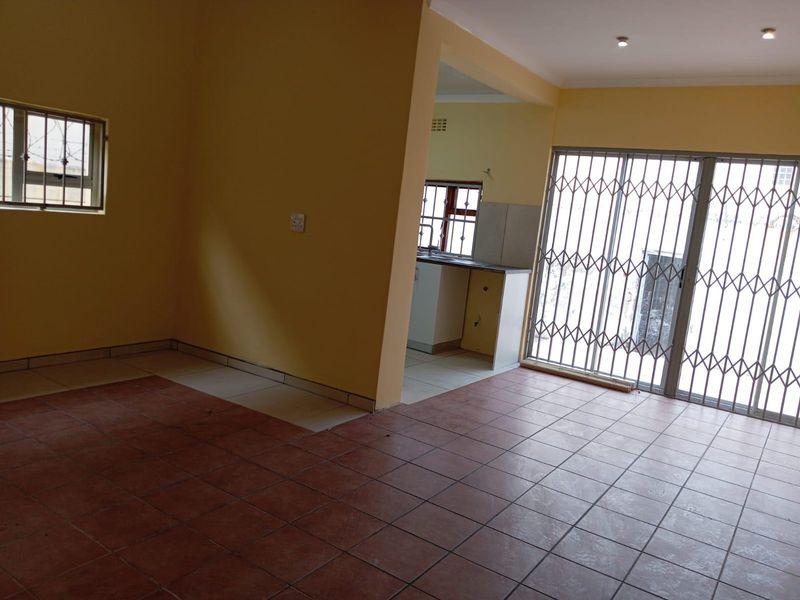 An open-plan living and kitchen area featuring tiled floors, security gates, and basic built-in cabinetry, offering a blank canvas for renovation.