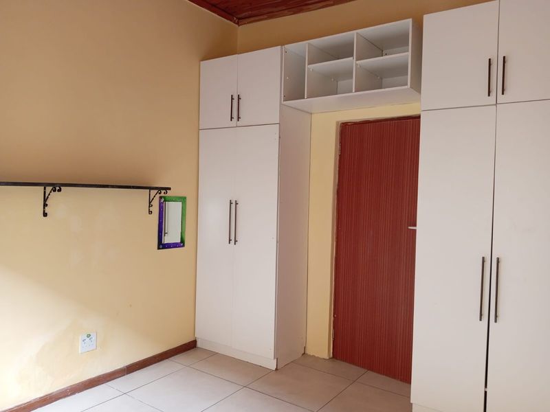 A bedroom featuring built-in white cupboards, tiled flooring, and a timber ceiling, offering a functional space ready for personalization.