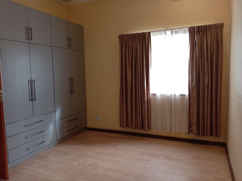A clean, empty bedroom featuring modern grey built-in cupboards, light-toned laminate flooring, and a window with installed curtain tracks.