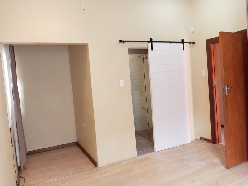 A vacant bedroom featuring laminate flooring, a modern white sliding barn door, and direct access to an en-suite shower area.