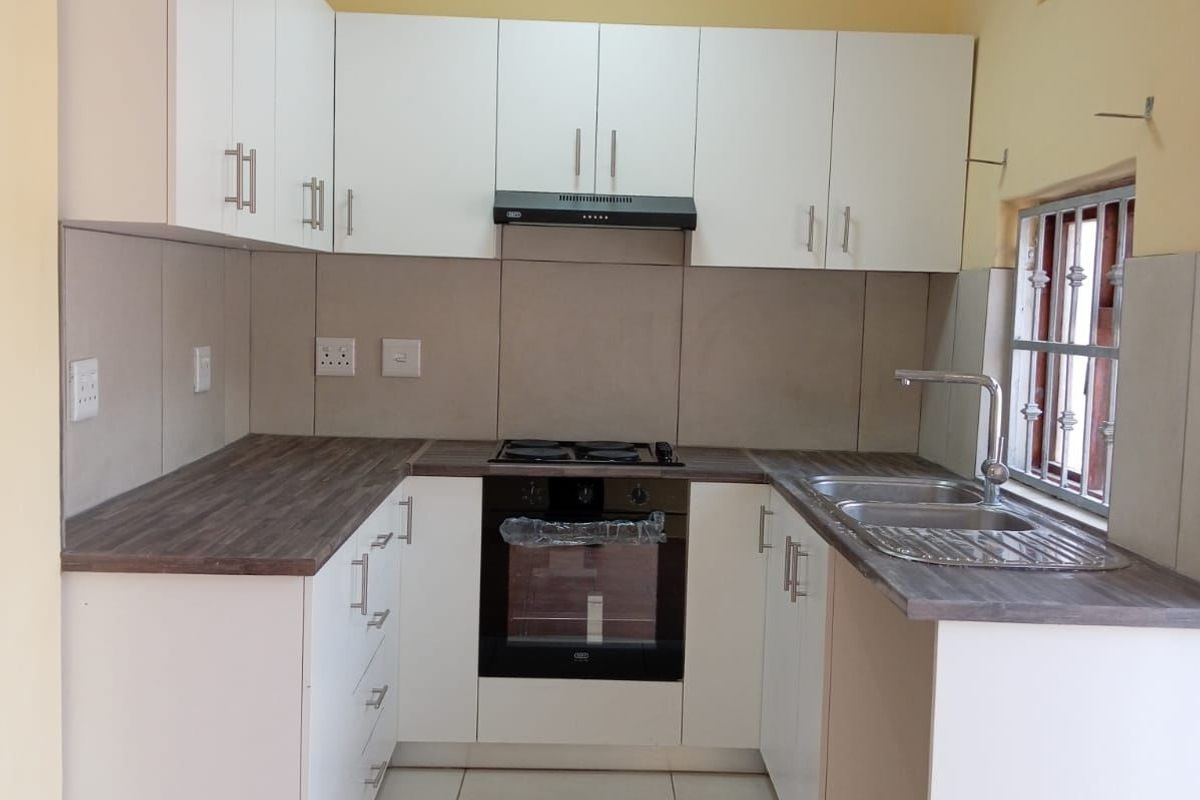 A clean, modern kitchen featuring white cabinetry, dark laminate countertops, built-in oven, gas hob, extractor fan, and a double sink with tiled flooring.