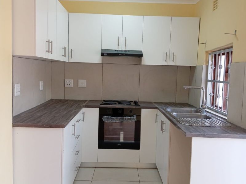 A clean, modern kitchen featuring white cabinetry, dark laminate countertops, built-in oven, gas hob, extractor fan, and a double sink with tiled flooring.