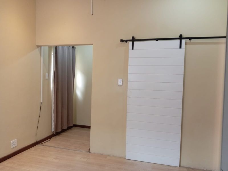 A neutral bedroom featuring light laminate flooring and a modern white sliding barn door, providing a clean and versatile space.