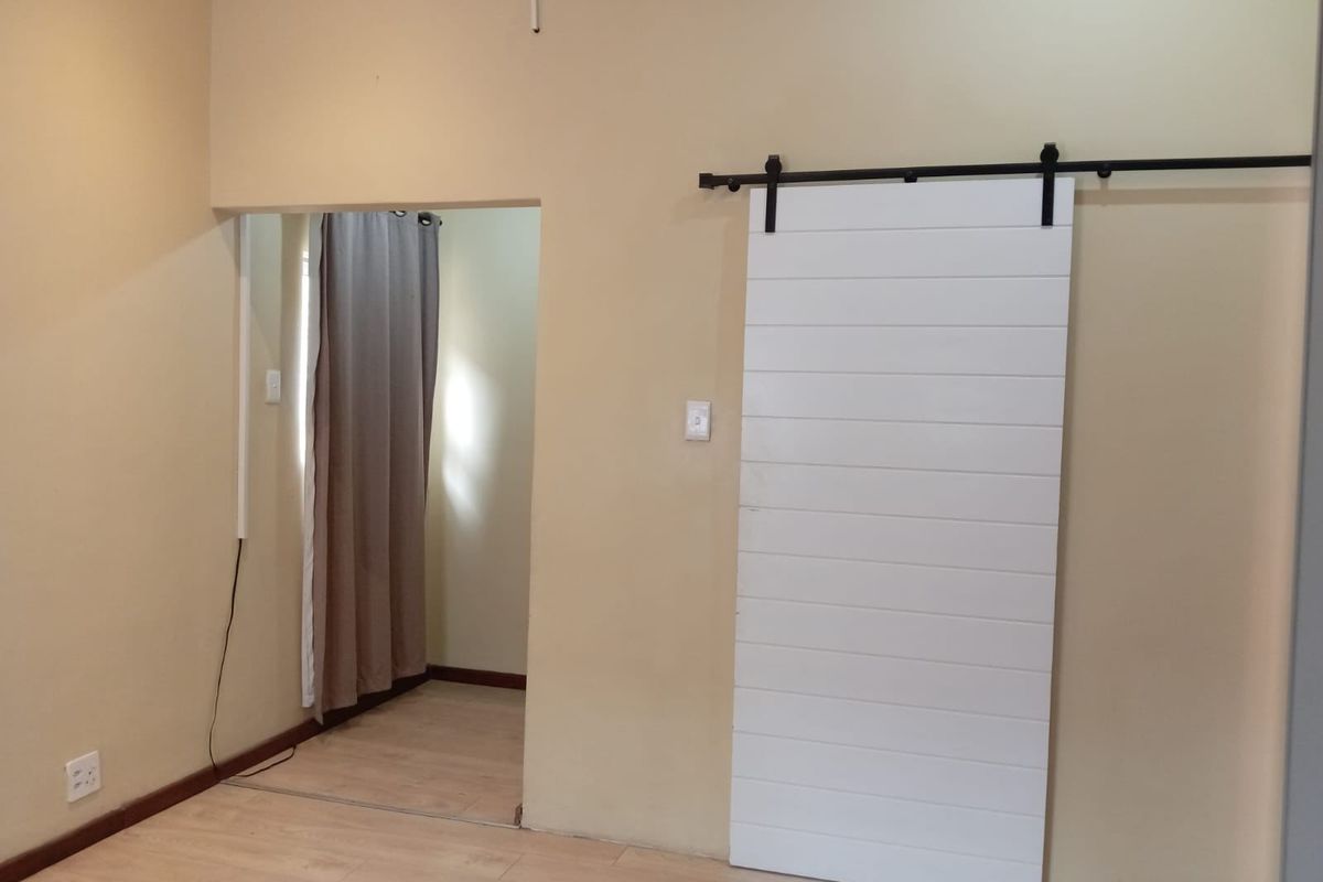 A neutral bedroom featuring light laminate flooring and a modern white sliding barn door, providing a clean and versatile space.