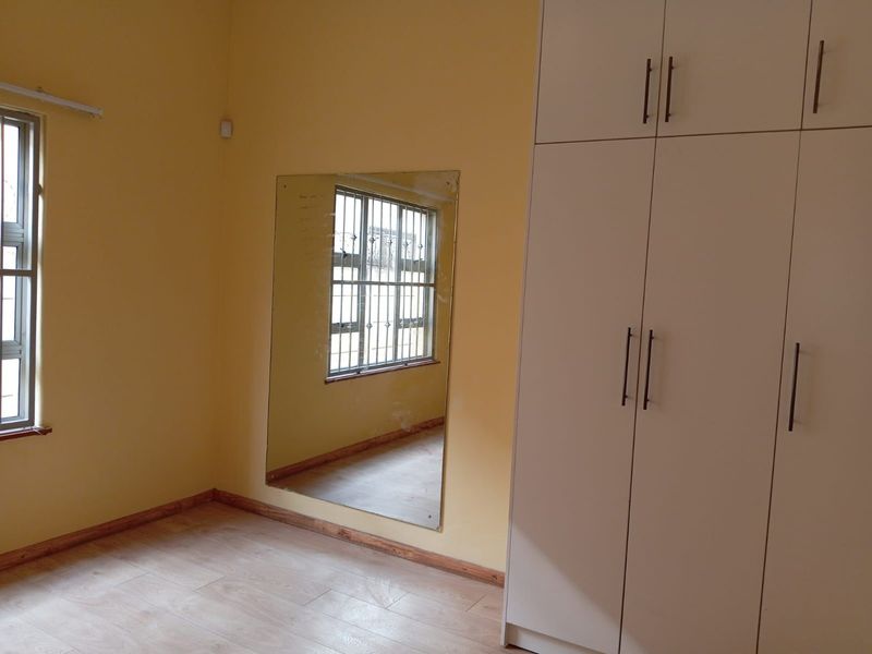 A vacant bedroom featuring light-toned laminate flooring, built-in white cabinetry, and security bars on the windows.
