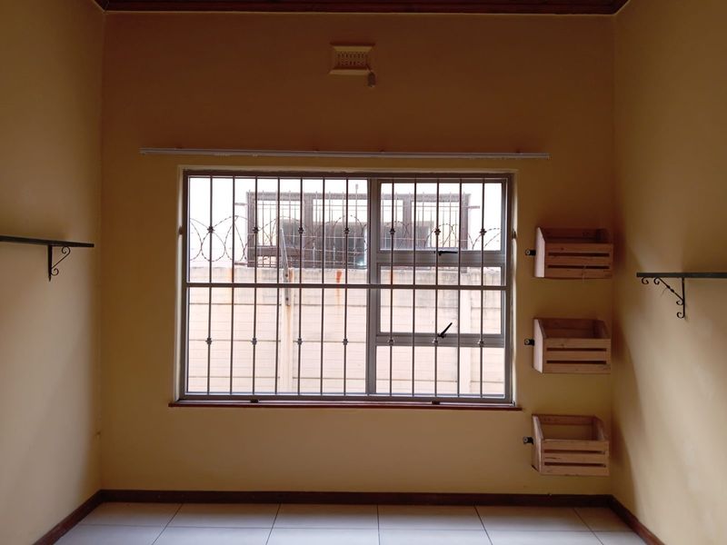 An empty bedroom featuring tiled flooring, a window with security bars, and a ventilation grille. The space is ready for a fresh coat of paint.