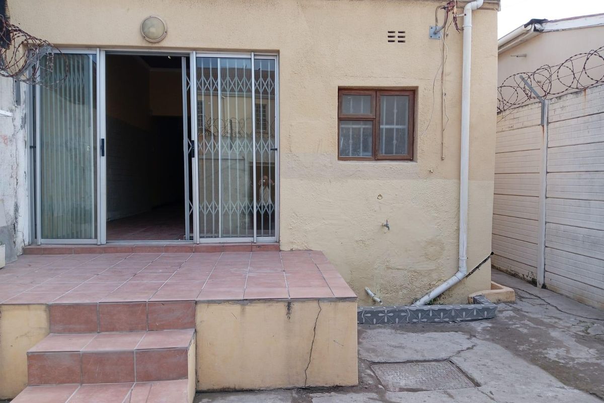 Rear exterior view showing a tiled patio, sliding door with security gate, and weathered wall finishes with visible structural cracking.