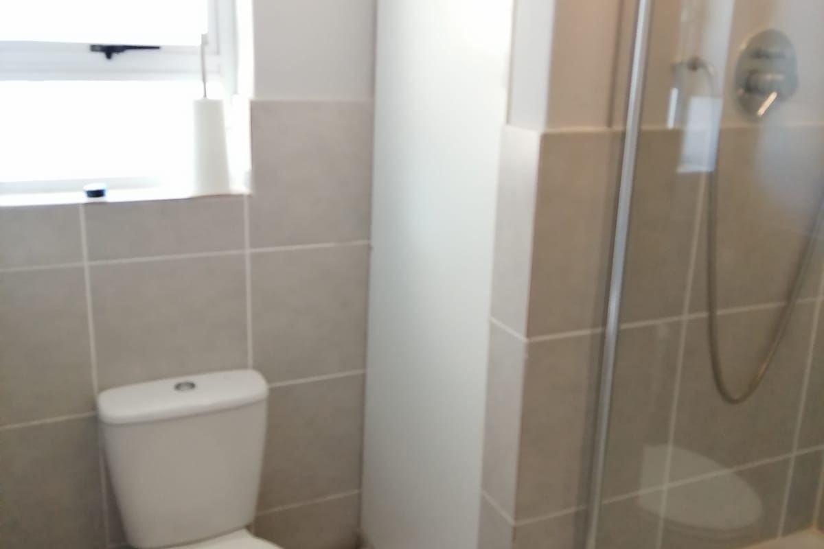 A functional bathroom featuring a shower enclosure, toilet, and basin with neutral wall and floor tiling.