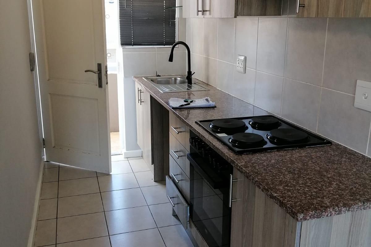 A compact kitchen featuring laminate cabinetry, granite countertops, a built-in oven with electric hob, and tiled flooring with direct access to an outdoor area.