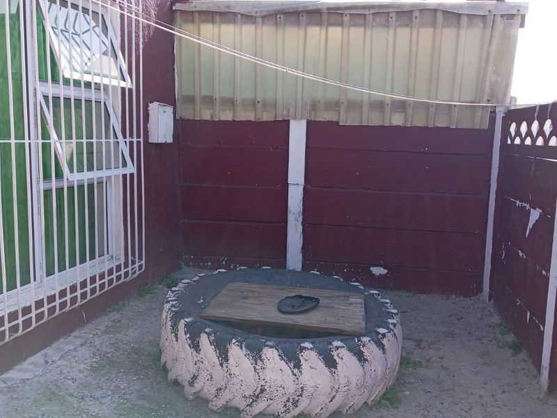 A small rear courtyard area featuring a concrete boundary wall, security bars on the window, and a basic concrete ground surface.