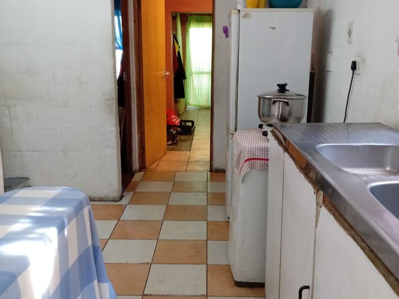 A dated kitchen area featuring tiled flooring, basic cabinetry, and a stainless steel sink, requiring cosmetic updates to improve its overall appeal.
