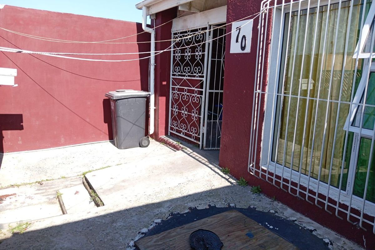 Rear exterior area featuring concrete paving, security gates, and security bars on windows, enclosed by a painted boundary wall.