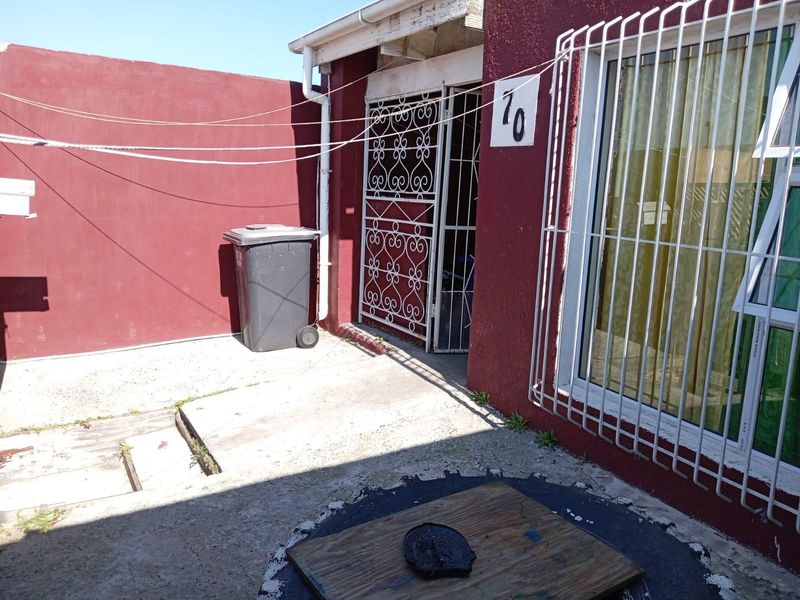 Rear exterior area featuring concrete paving, security gates, and security bars on windows, enclosed by a painted boundary wall.