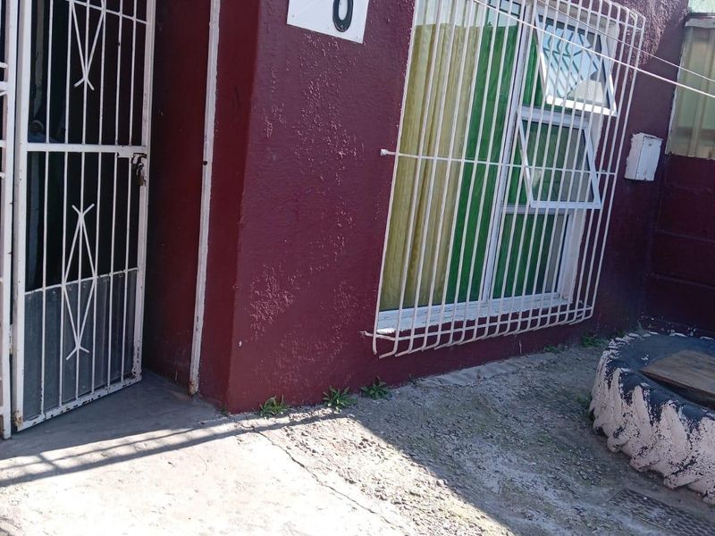 Front entrance view of the property featuring a security gate, protective window bars, and a concrete walkway.