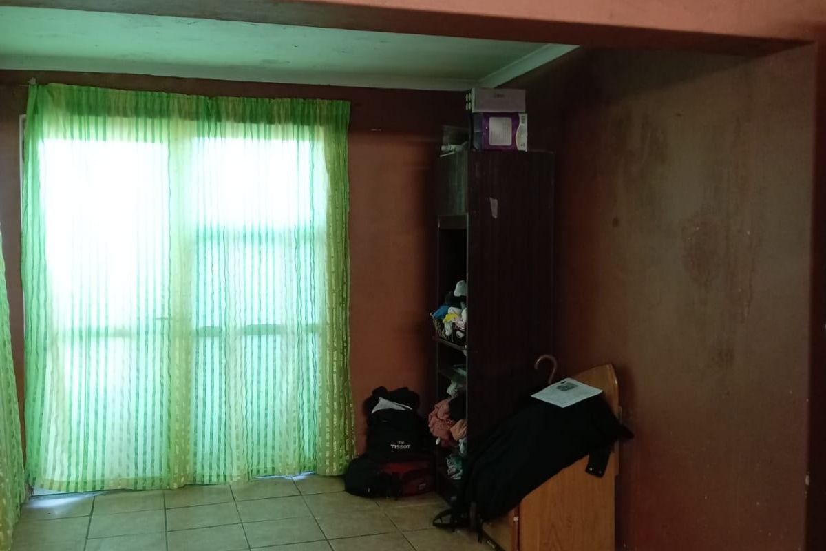A living area featuring ceramic floor tiles and a sliding glass door, currently showing signs of wear and requiring cosmetic updates.