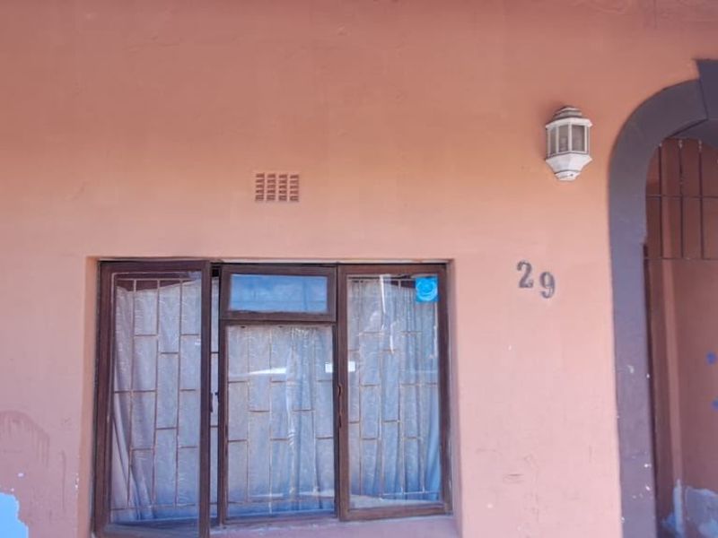 Front facade of the property featuring an arched entrance, security gate, and window security bars, showing signs of exterior wear.