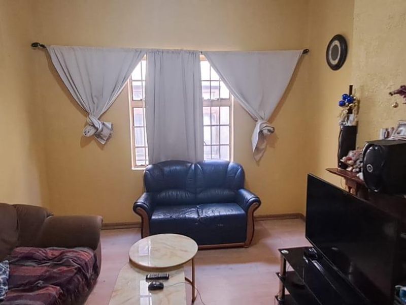 A living room featuring a central window with curtain rods and textured yellow walls, requiring cosmetic updates to improve the overall aesthetic.
