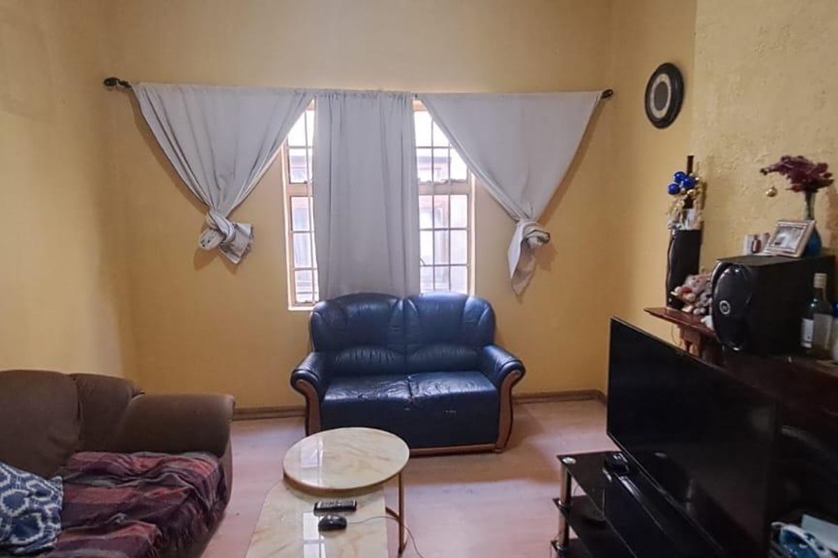 A living room featuring a central window with curtain rods and textured yellow walls, requiring cosmetic updates to improve the overall aesthetic.