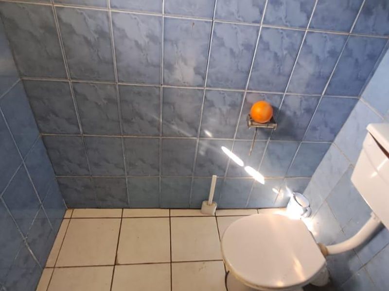 A small bathroom featuring blue wall tiles and white floor tiles, equipped with a standard toilet and exposed plumbing fixtures.