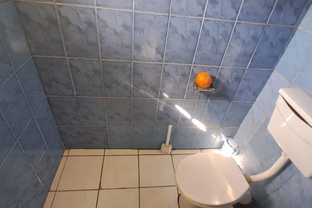 A small bathroom featuring blue wall tiles and white floor tiles, equipped with a standard toilet and exposed plumbing fixtures.