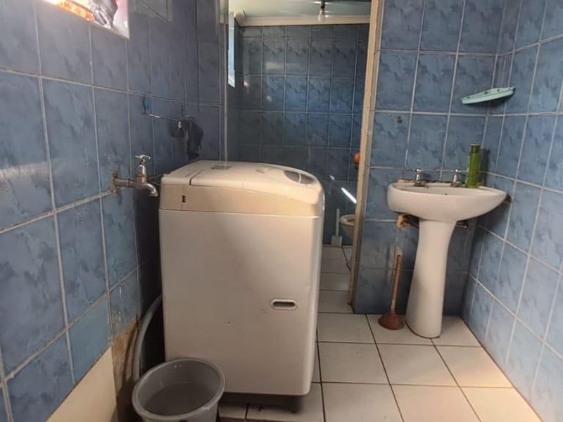 A functional laundry area featuring fully tiled walls, a pedestal basin, and plumbing connections for a washing machine.