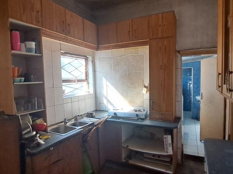A dated kitchen featuring wooden cabinetry, a double sink, and tiled splashbacks, requiring renovation to modernize the space and improve functionality.