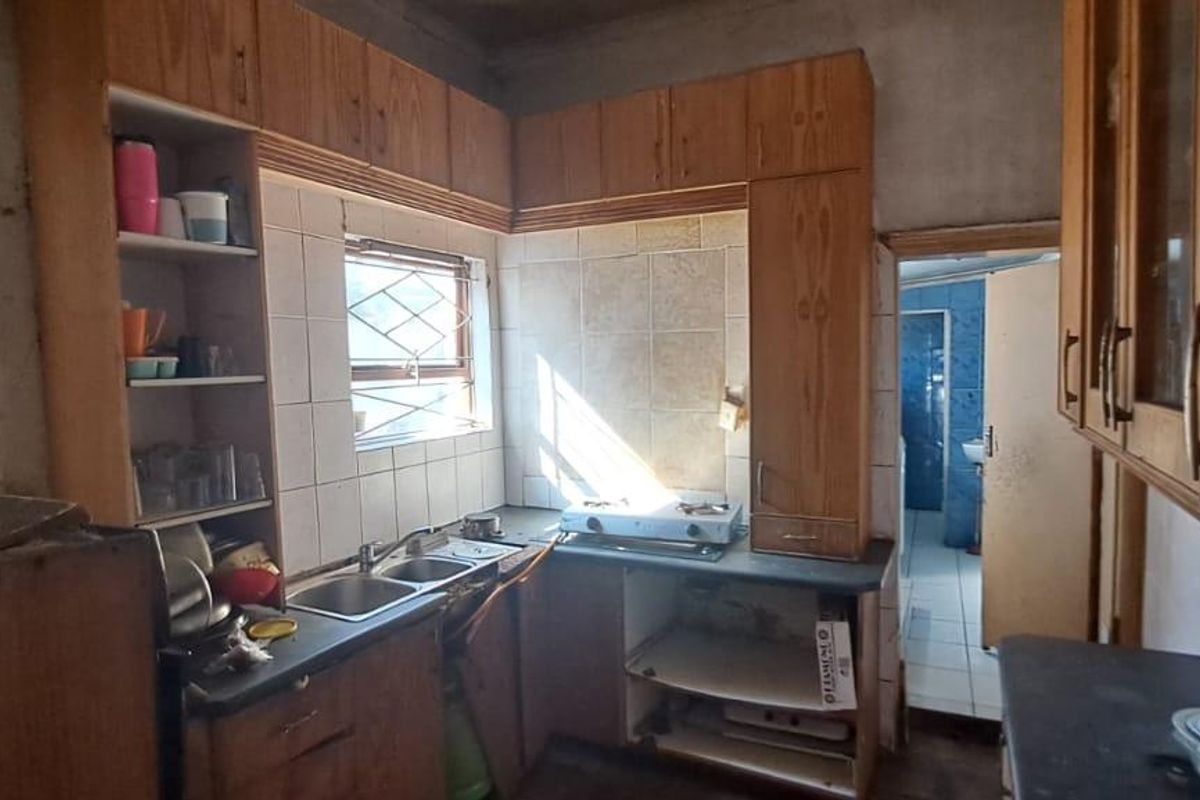 A dated kitchen featuring wooden cabinetry, a double sink, and tiled splashbacks, requiring renovation to modernize the space and improve functionality.