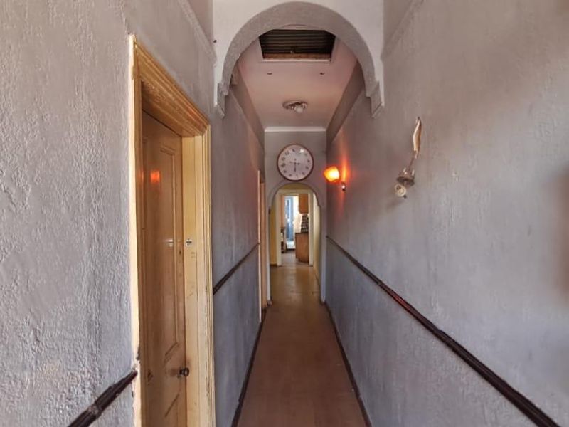 A narrow residential hallway featuring an arched transition, timber door, and dado rail, currently showing signs of wear and requiring cosmetic refurbishment.