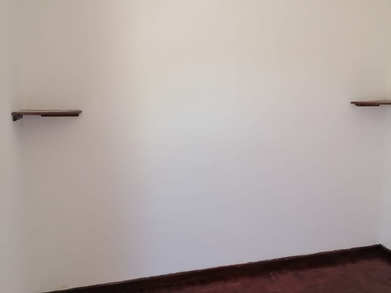 An empty bedroom featuring dark parquet flooring, two wall-mounted shelves, and a high-level air vent.