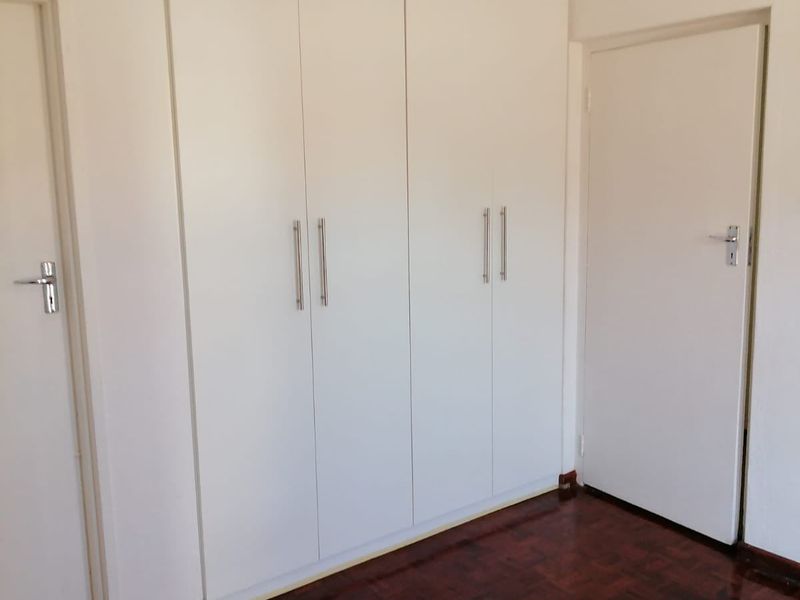 A clean, empty bedroom featuring polished parquet flooring and white built-in cupboards with modern handles.