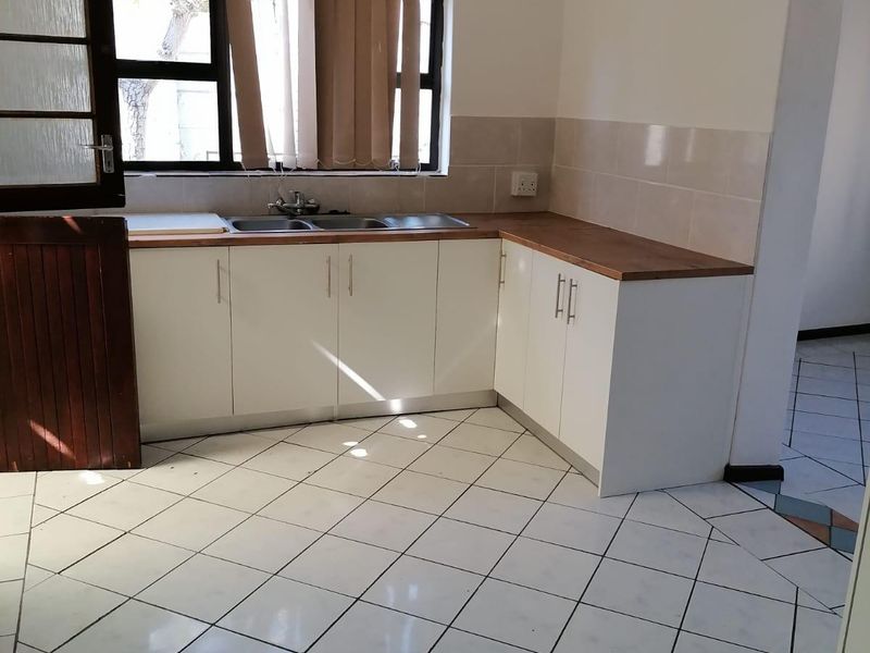 A functional kitchen featuring white built-in cabinetry, a laminate countertop, double basin sink, and tiled flooring throughout.
