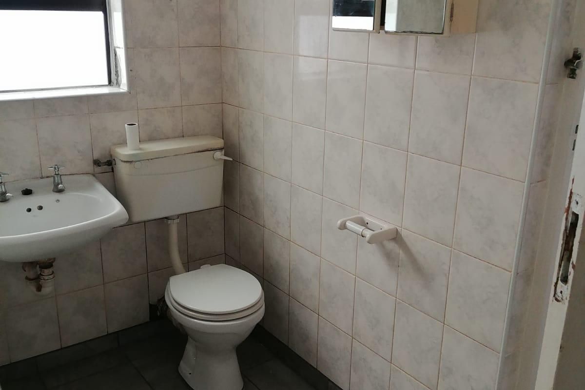 A functional bathroom featuring tiled walls and floors, a pedestal basin, and a standard toilet, ready for modernization.