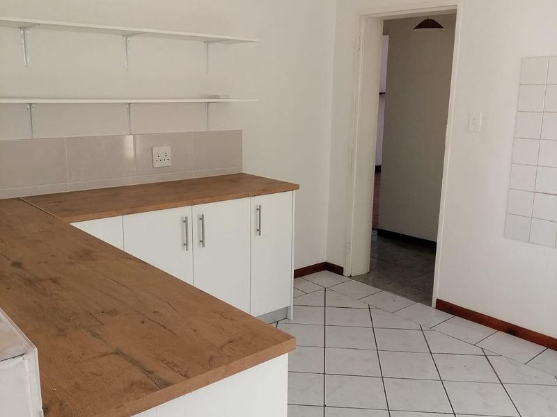 A clean, empty kitchen area featuring modern white cabinetry, wooden countertops, tiled flooring, and wall-mounted shelving, offering a functional and neutral space.