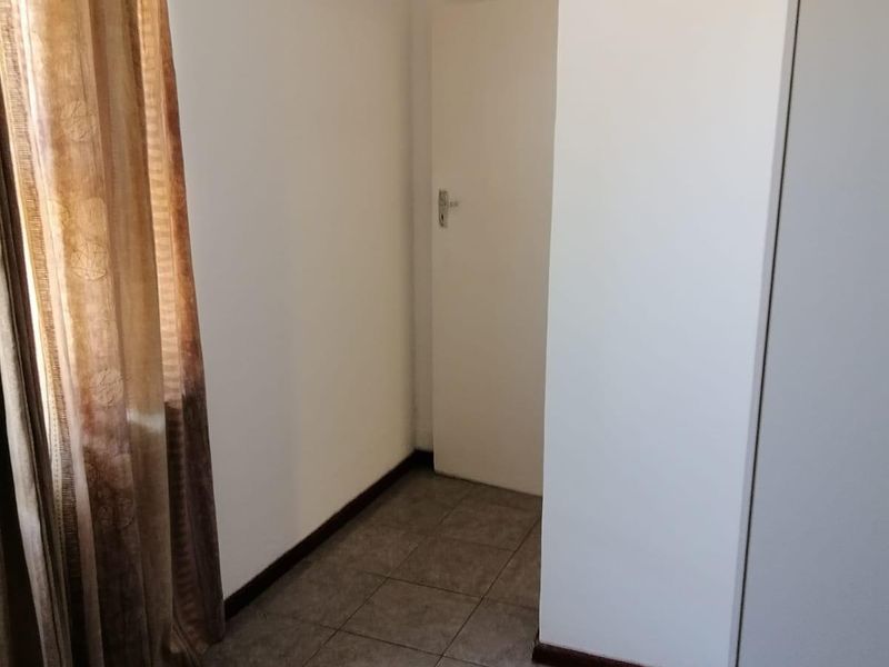 A clean, empty bedroom featuring neutral tiled flooring and a built-in cupboard, offering a blank canvas for personalization.