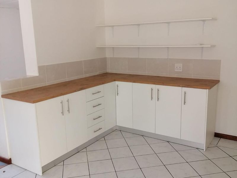 A clean, empty kitchen area featuring white cabinetry, wooden countertops, tiled backsplash, and wall-mounted shelving, ready for customization.