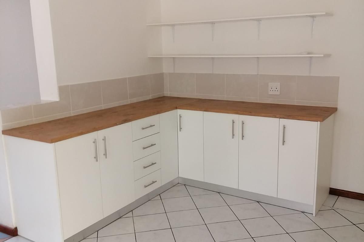 A clean, empty kitchen area featuring white cabinetry, wooden countertops, tiled backsplash, and wall-mounted shelving, ready for customization.