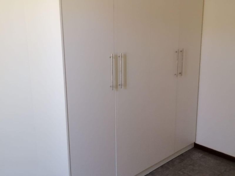 A clean, empty bedroom featuring neutral tiled flooring and a large, modern built-in wardrobe with sleek handles.